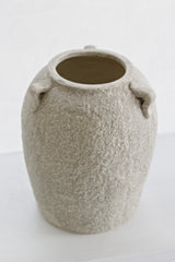 Beige stone vase displayed in bright window light on a white surface, minimal styling