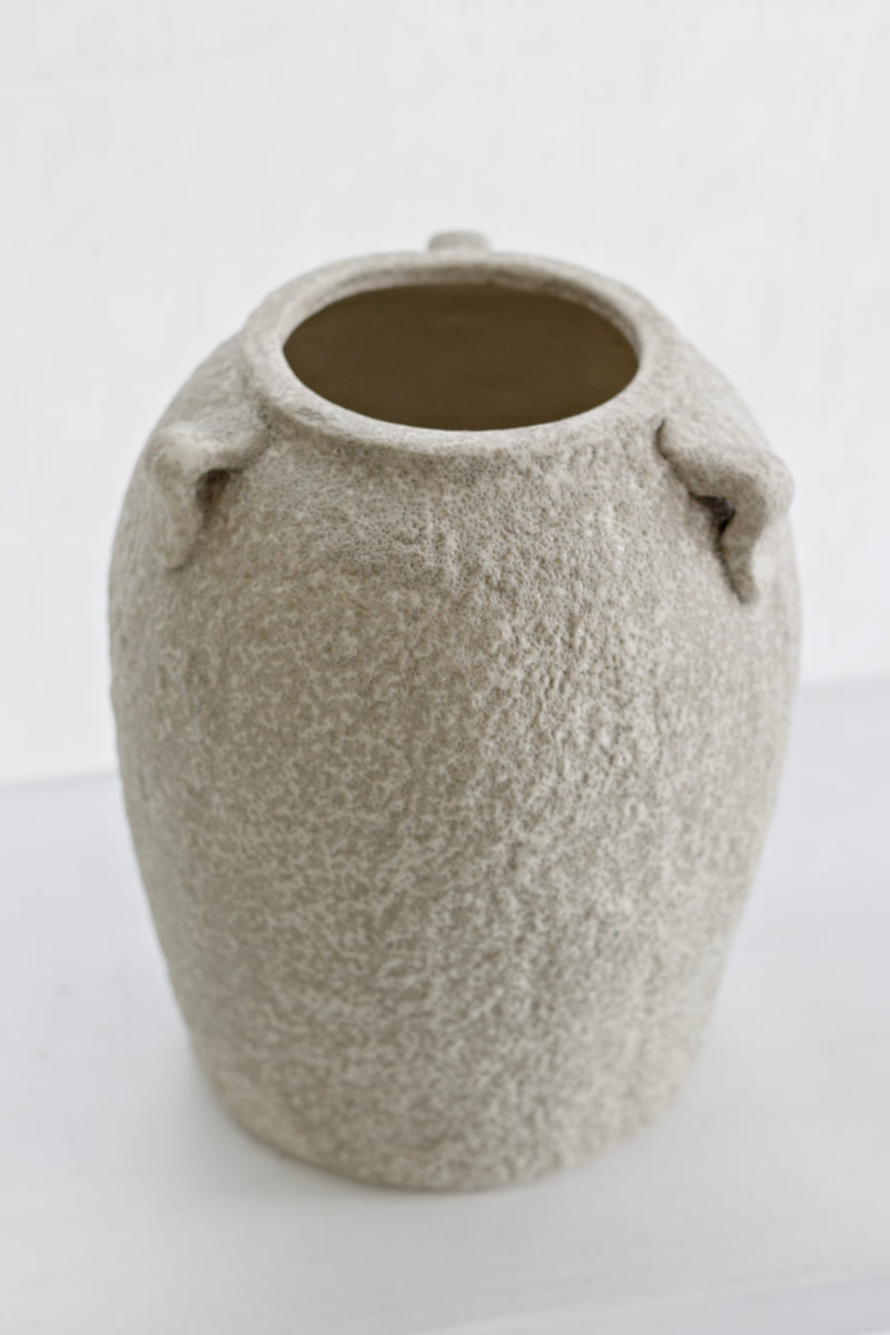 Beige stone vase displayed in bright window light on a white surface, minimal styling
