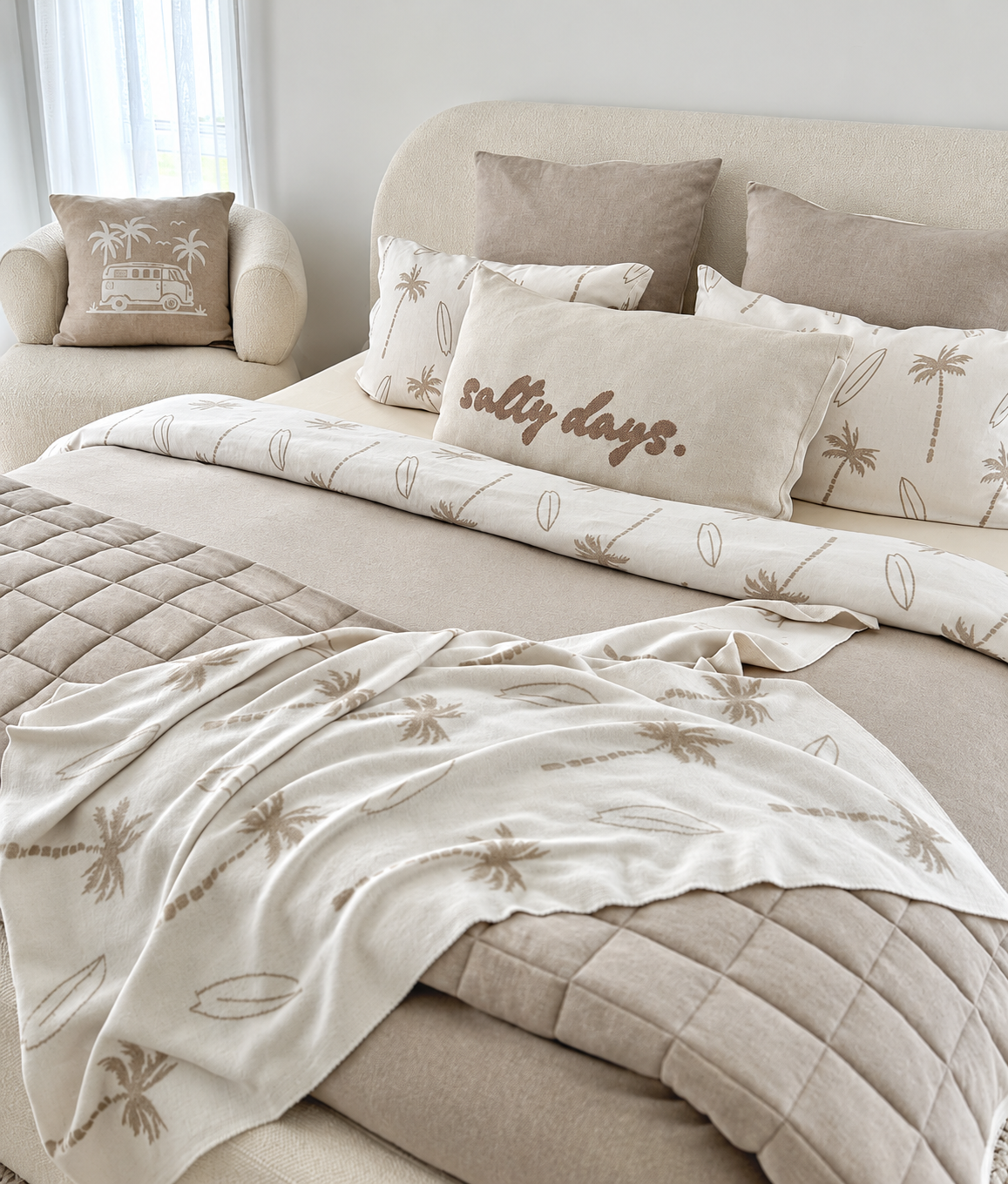 Bengali Collections palm and surfboard print duvet cover, pillowcases and throw on a boucle bed with a salty days cushion, beside an armchair with a campervan cushion