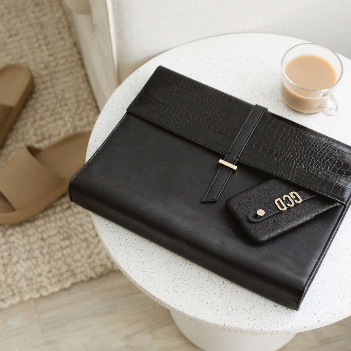 Black Penelope laptop sleeve on a white table with a coffee