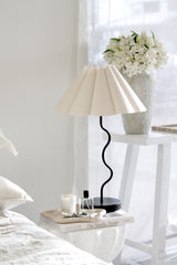 Black wavy table lamp with pleated shade styled on bedside table