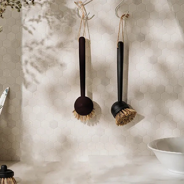 Two black-handled dish brushes hanging against a pale wall