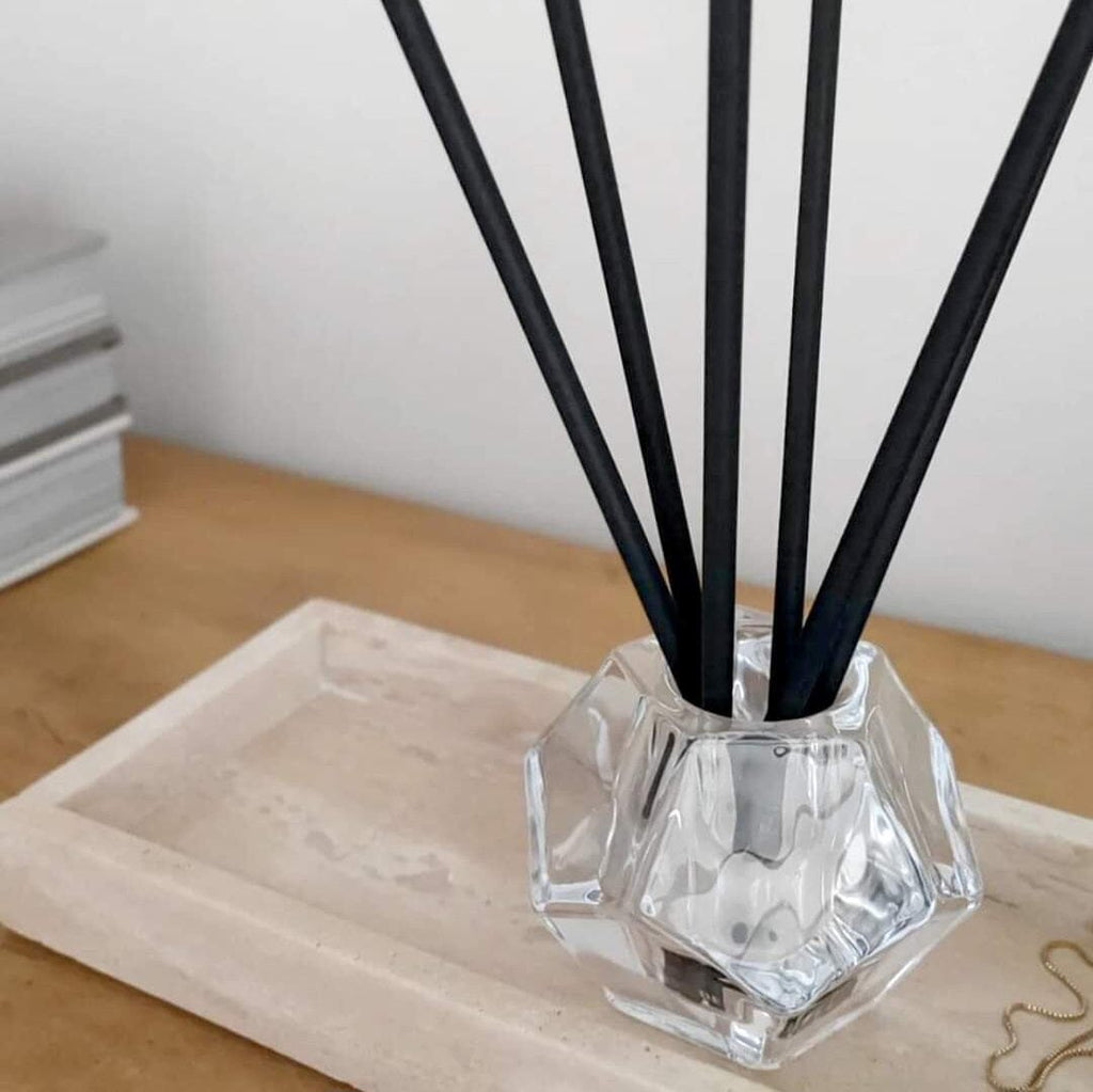 Aroma sticks in a faceted glass holder on a travertine tray with books behind