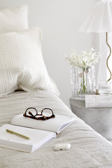 Tortoiseshell blue light filter glasses resting on an open journal on a neutral linen bed with cosy minimal styling.