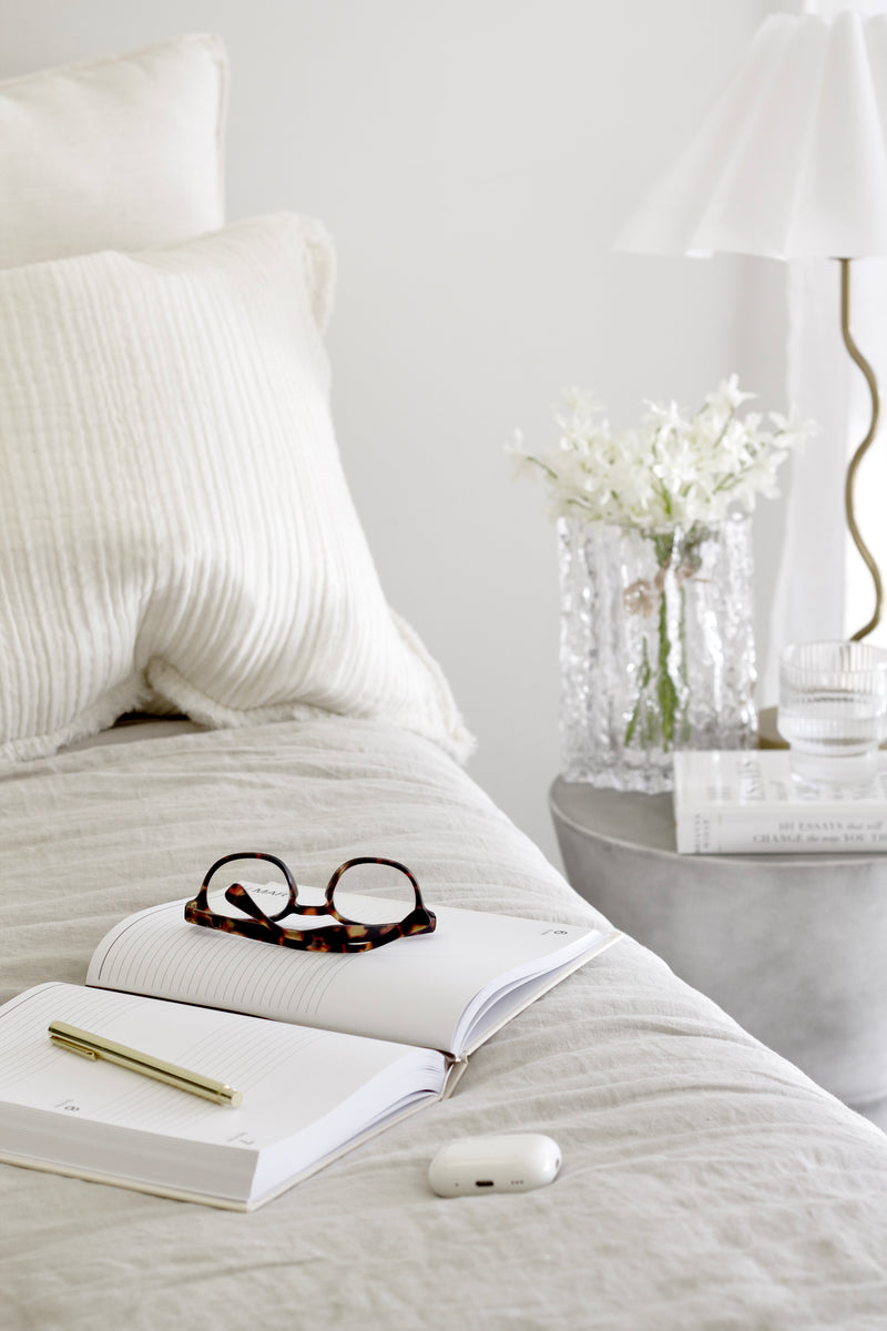 Tortoiseshell blue light filter glasses resting on an open journal on a neutral linen bed with cosy minimal styling.