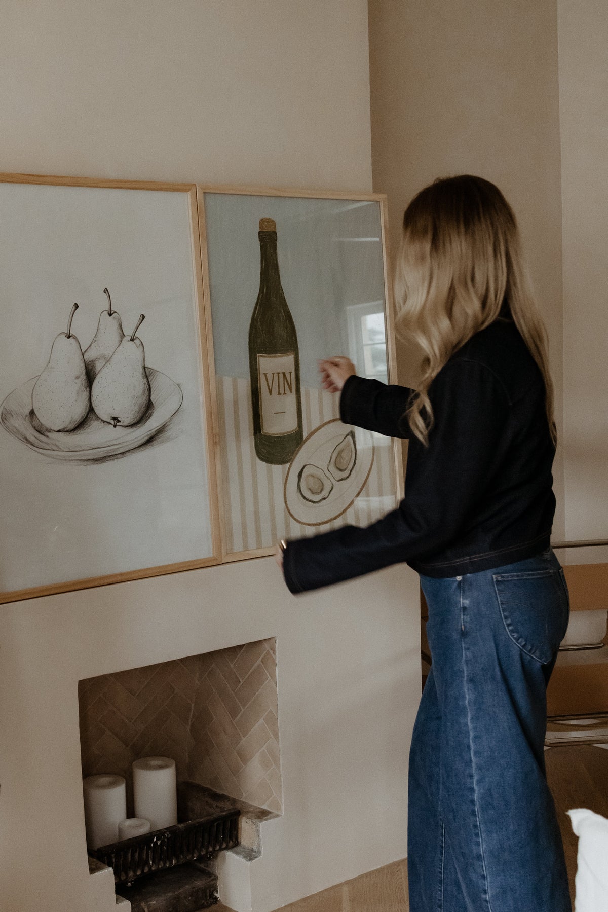 Woman hanging the Bol de Fruits print in a natural frame above a fireplace