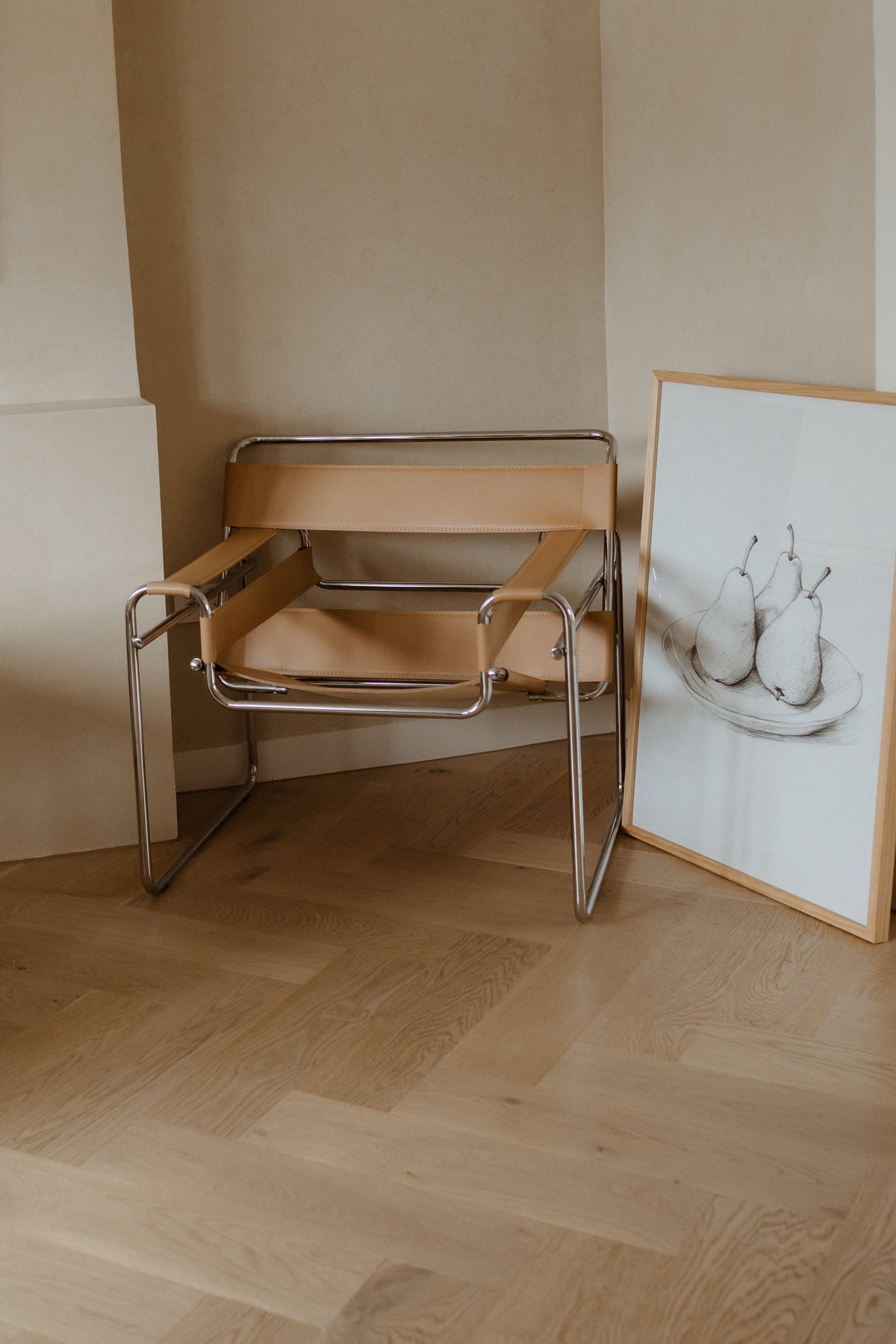 Bol de Fruits print in a natural frame leaning on a timber floor beside a leather and chrome chair