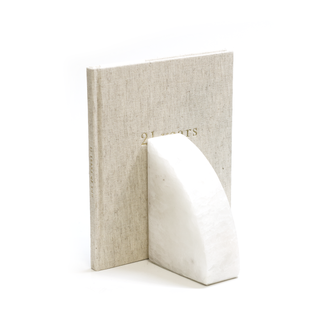 Solid marble rounded bookends holding linen journals on a shelf