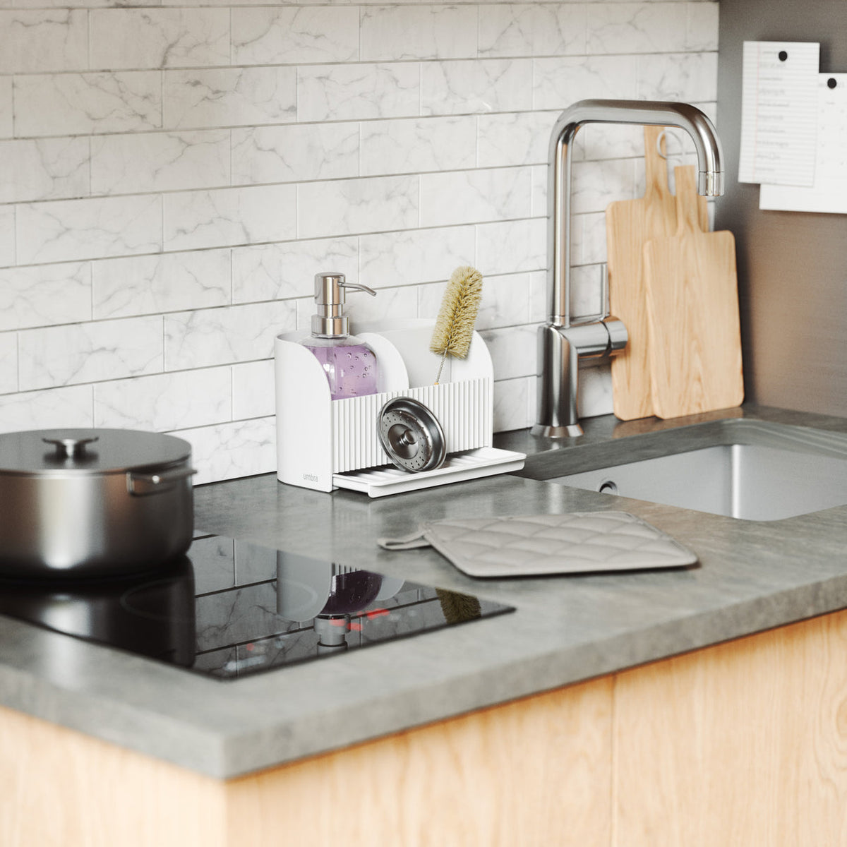 Umbra Sling sink caddy in white beside a kitchen sink with a soap pump and brush