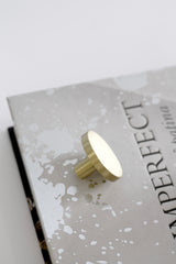 Brushed gold brass wall hook with round face styled on neutral book surface
