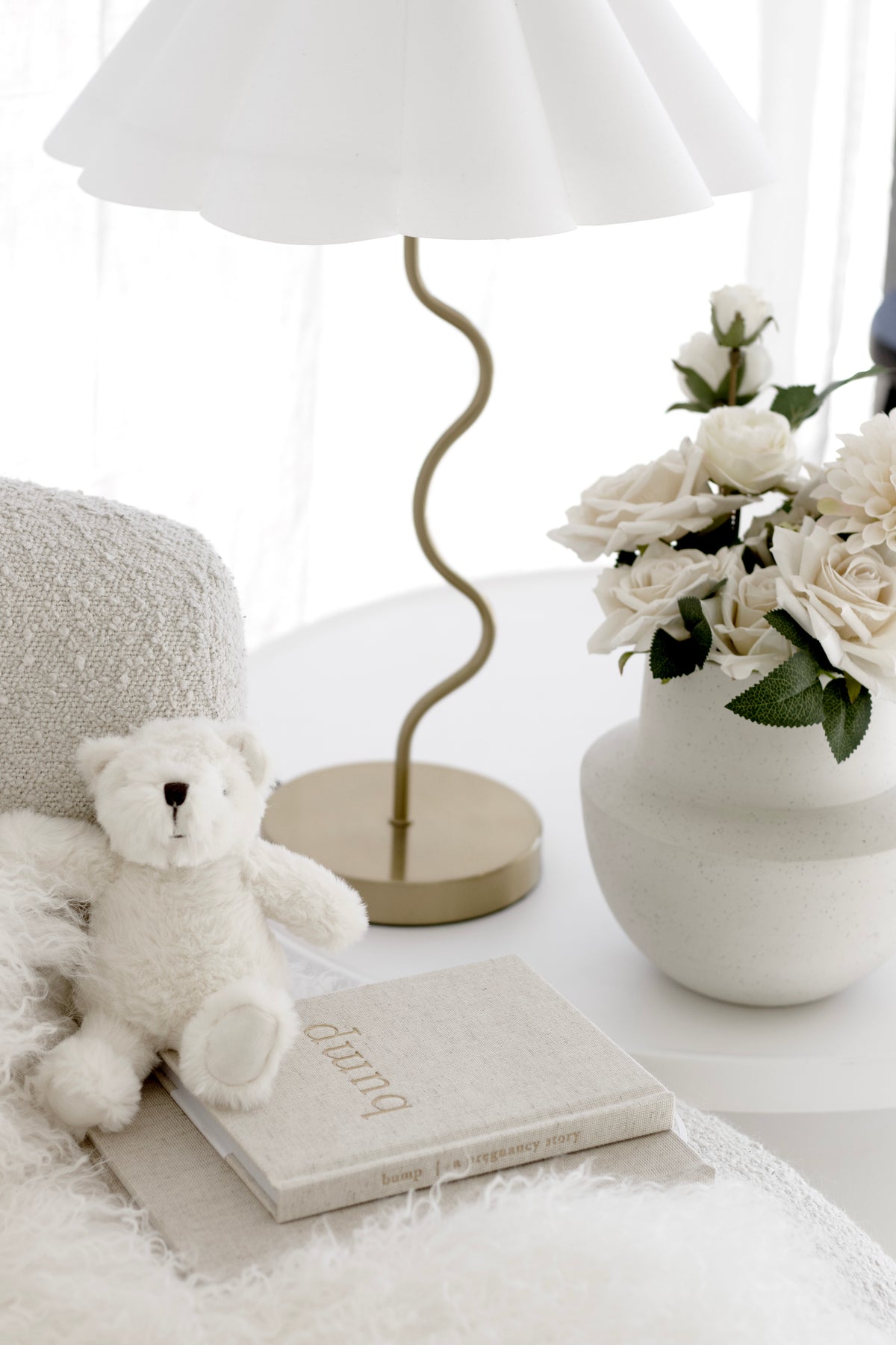 Bump pregnancy journal on a white side table with a teddy bear, white roses and a wavy gold lamp