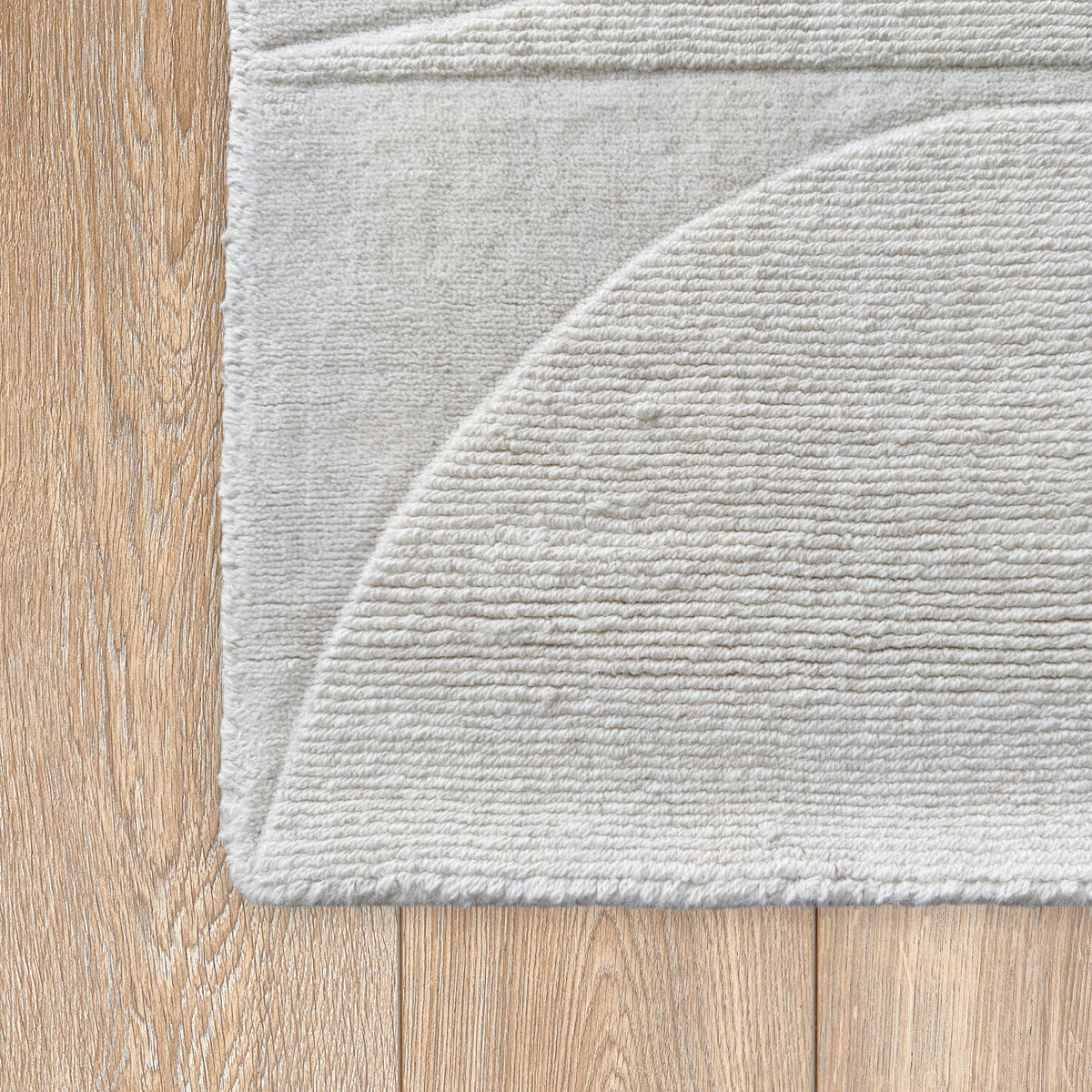 Corner of the ivory wool rug showing a raised semi-circle on a timber floor