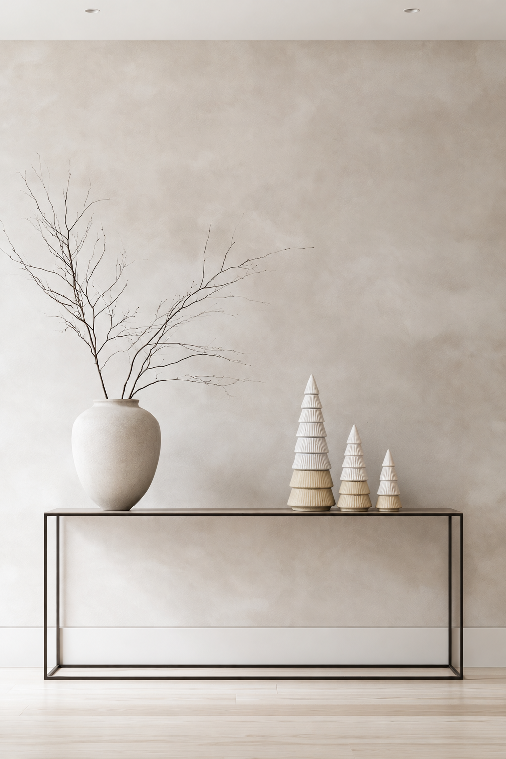 Ceramic Christmas Trees in three sizes grouped on a slim black console beside a stone vase of bare branches