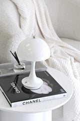 Chanel Collections and Creations book styled with a white mushroom lamp on a soft neutral bedside table.