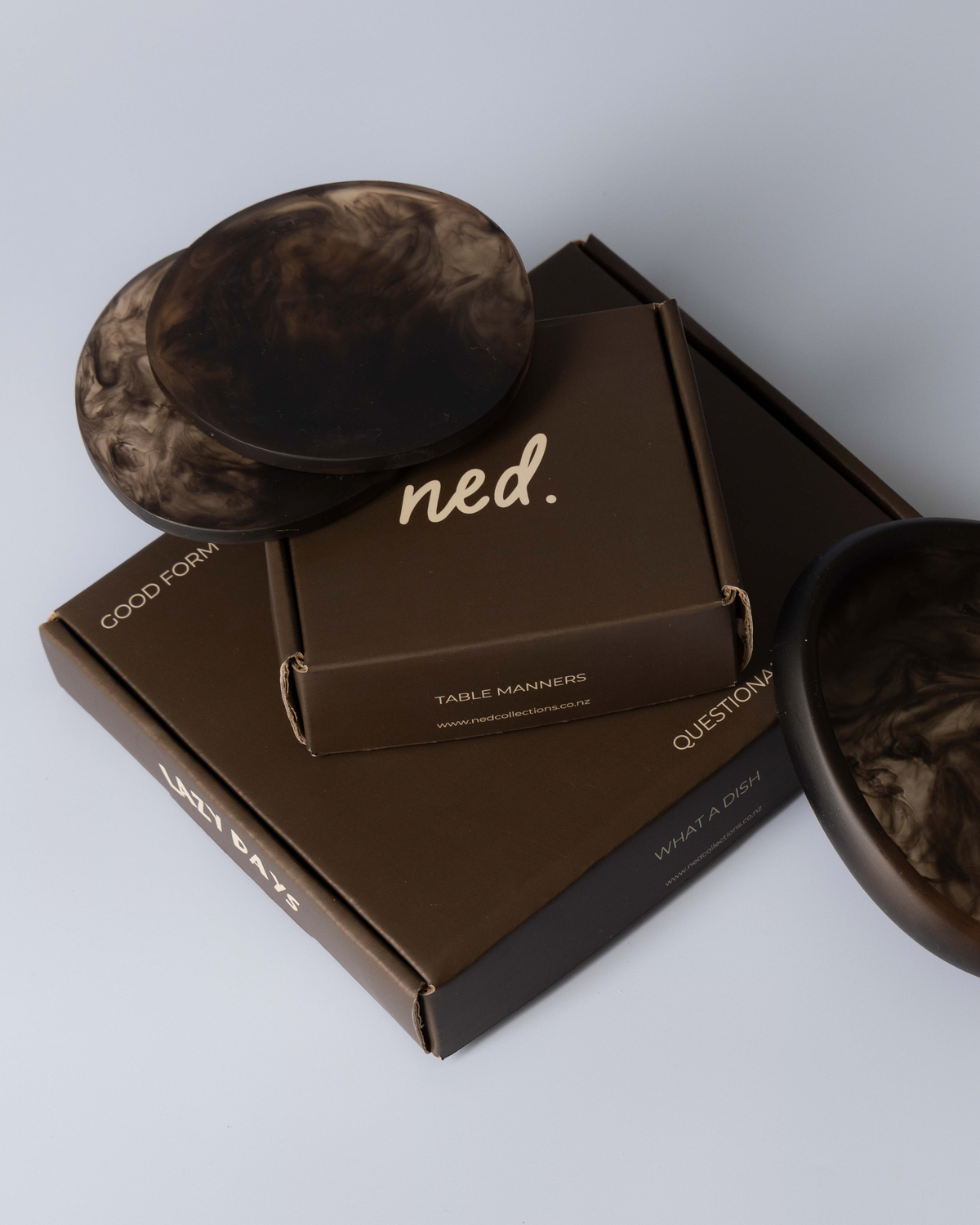 Chocolate resin coasters resting on stacked dark brown gift boxes beside a matching small bowl