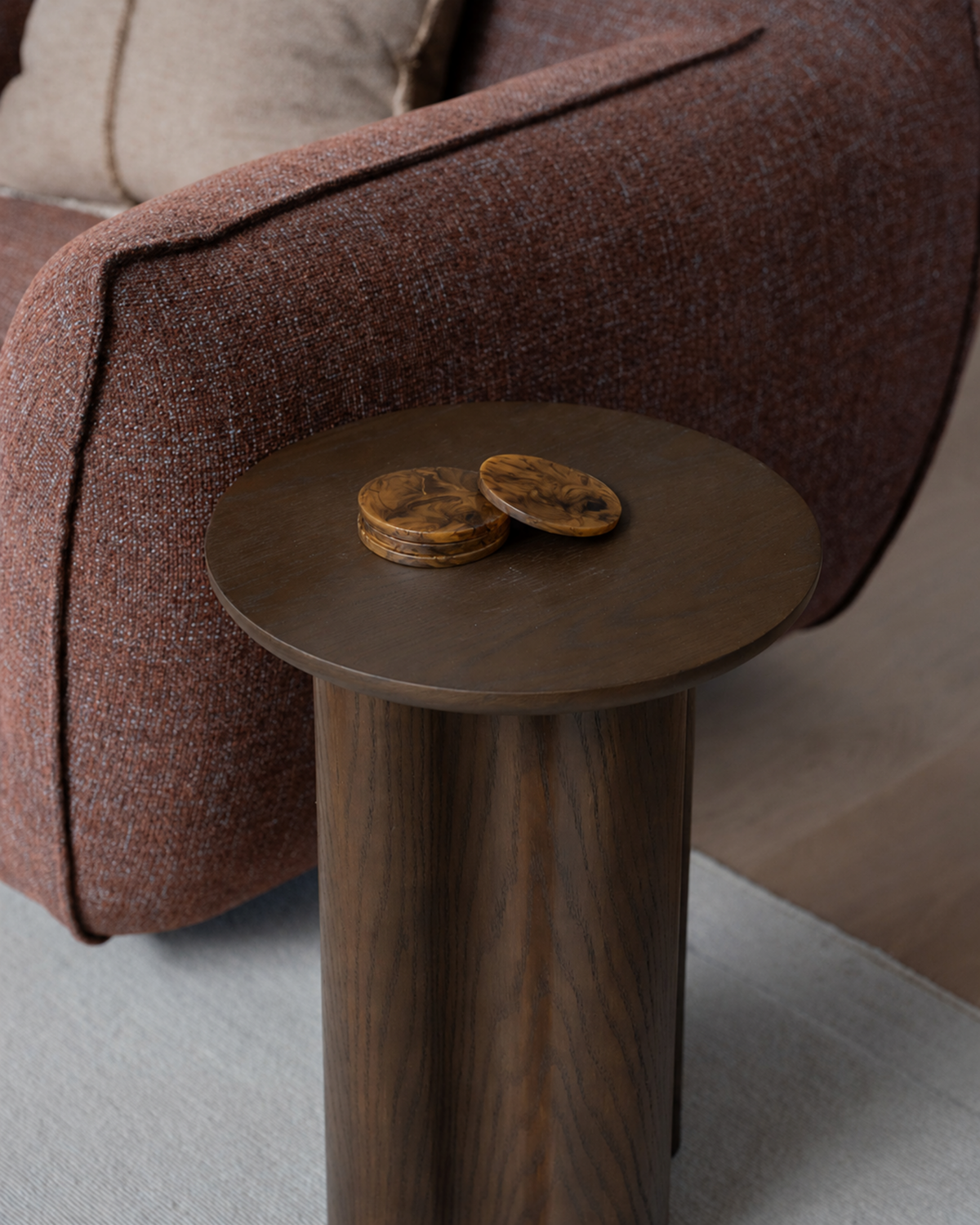 Brown marbled resin coasters stacked on a timber side table next to a rust tweed armchair