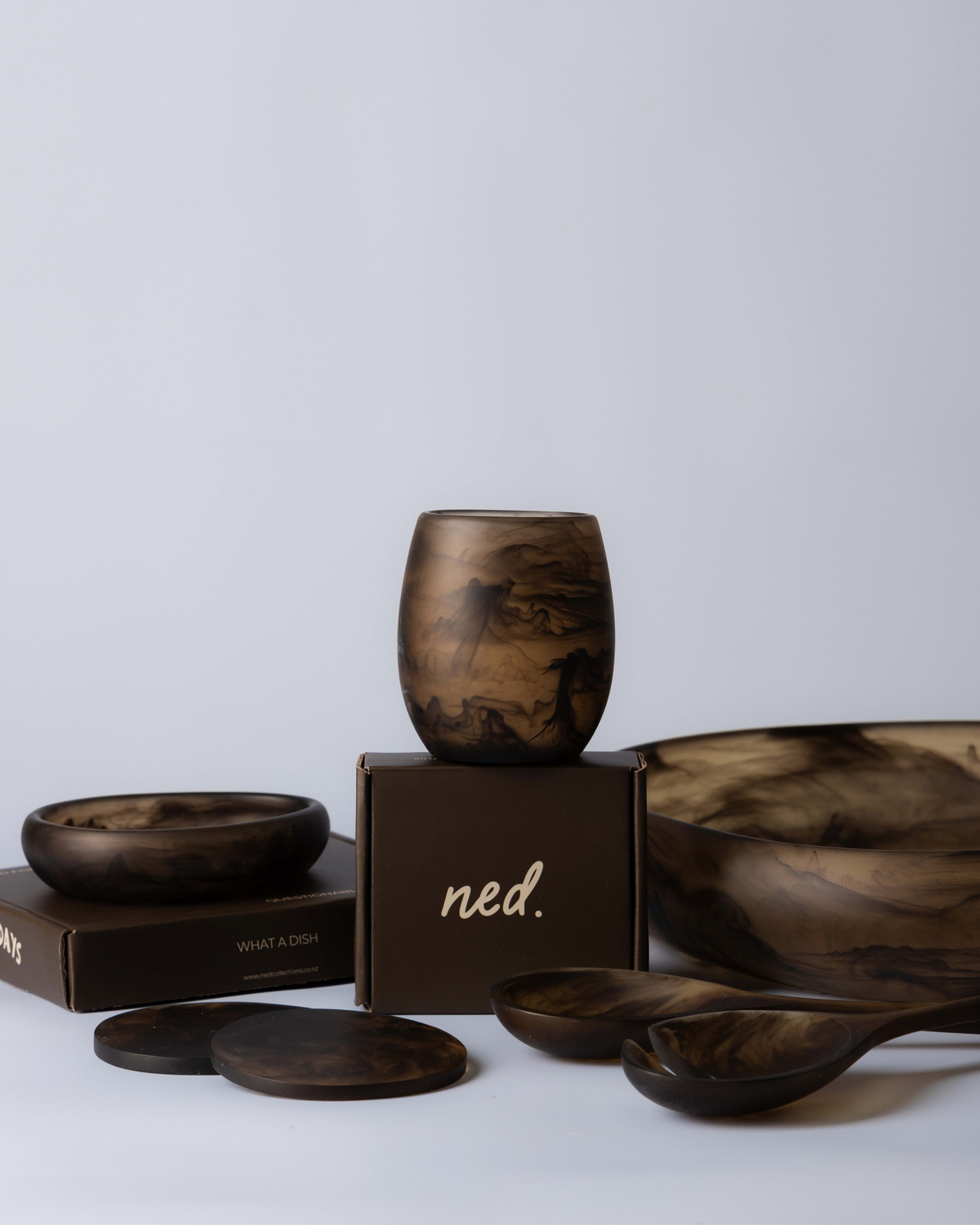 Chocolate small bowl in front of a gift box topped with a tumbler, with coasters, servers and a large bowl