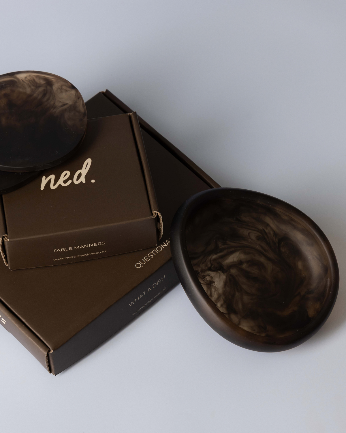 Chocolate small bowl leaning against stacked gift boxes with matching marbled resin coasters