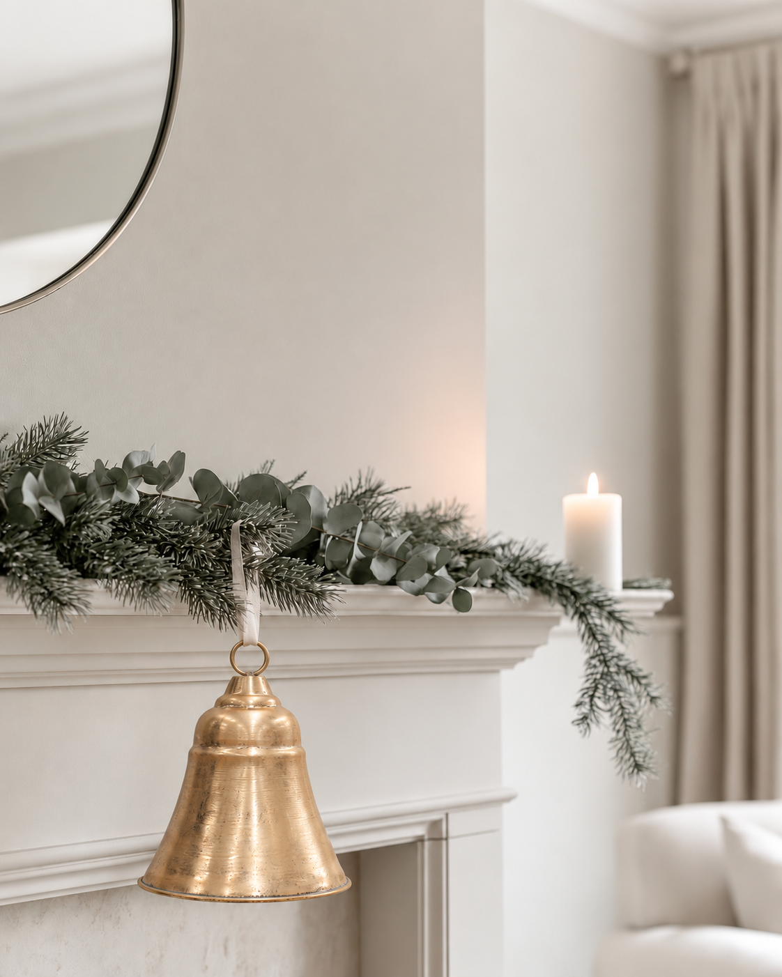 Chorus Bell in soft gold hanging from a white mantel with a eucalyptus and pine garland and a pillar candle