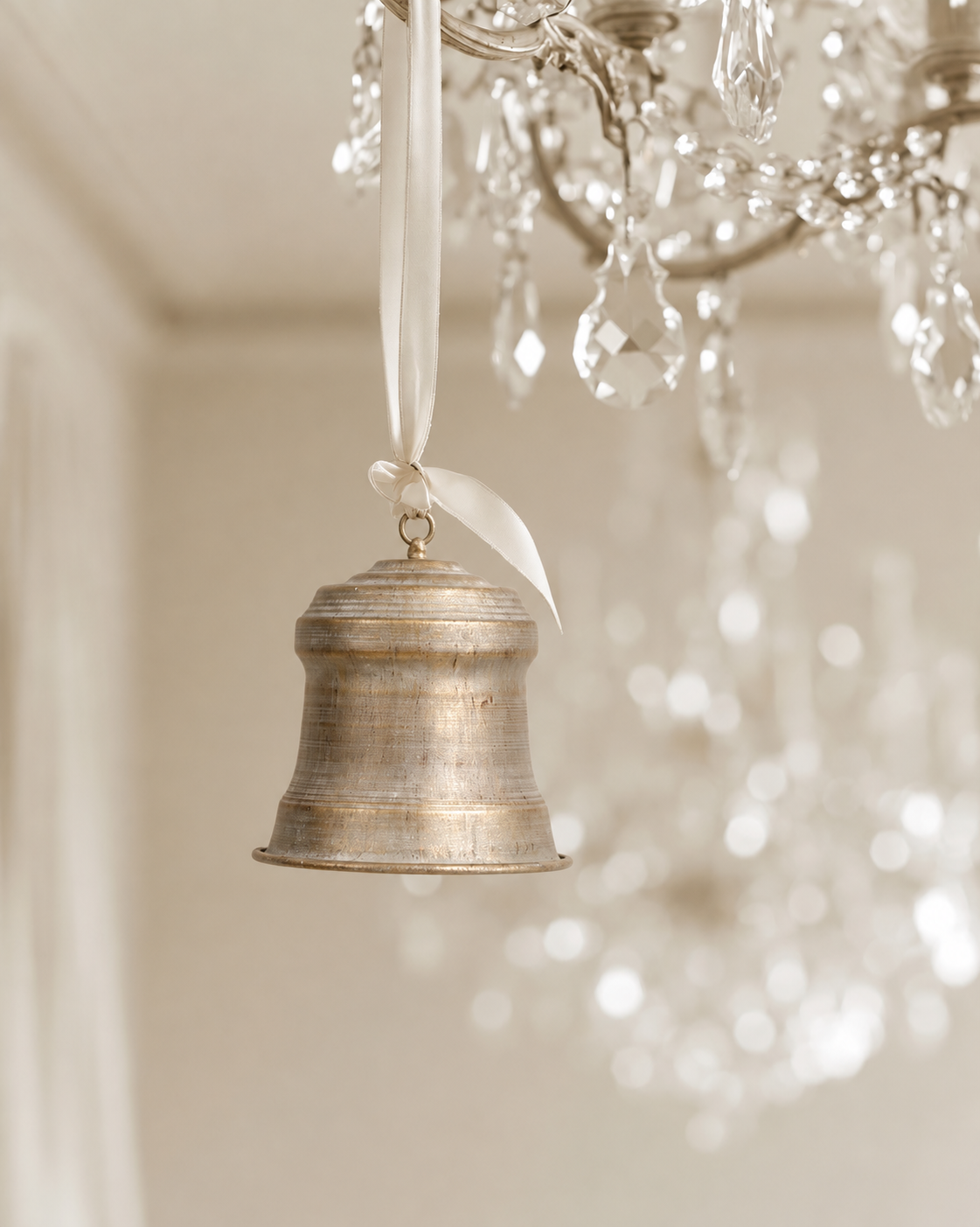 Church bell in brushed champagne hanging on a cream ribbon below a crystal chandelier