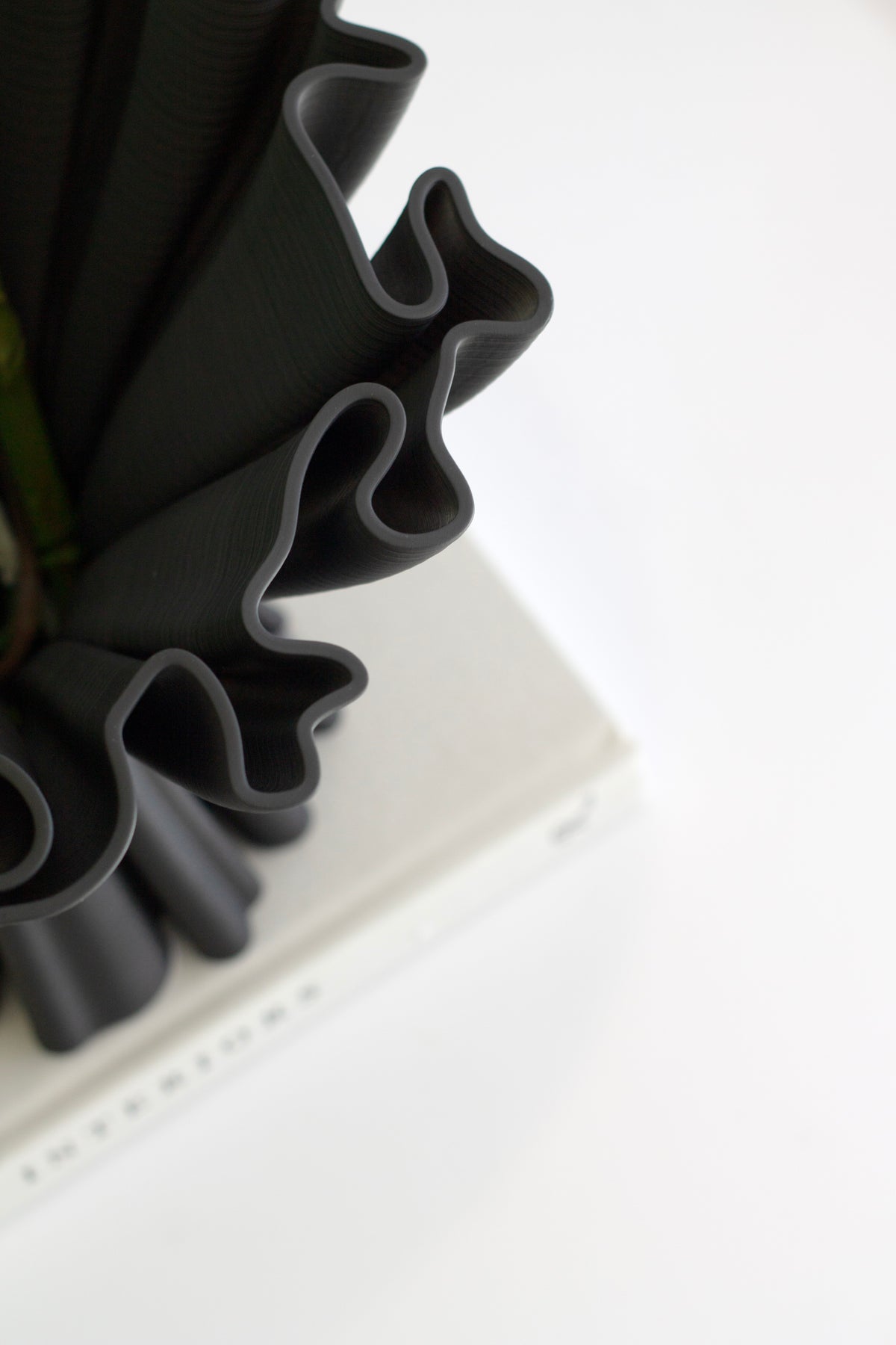 Close-up of the black Cleo compote vase's ruffled rim, with a book in the background