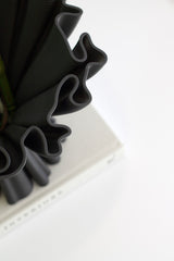 Close-up of the Cleo 3D printed compote vase in black with a sculptural ruffled rim, styled in a minimal setting with a book in the background