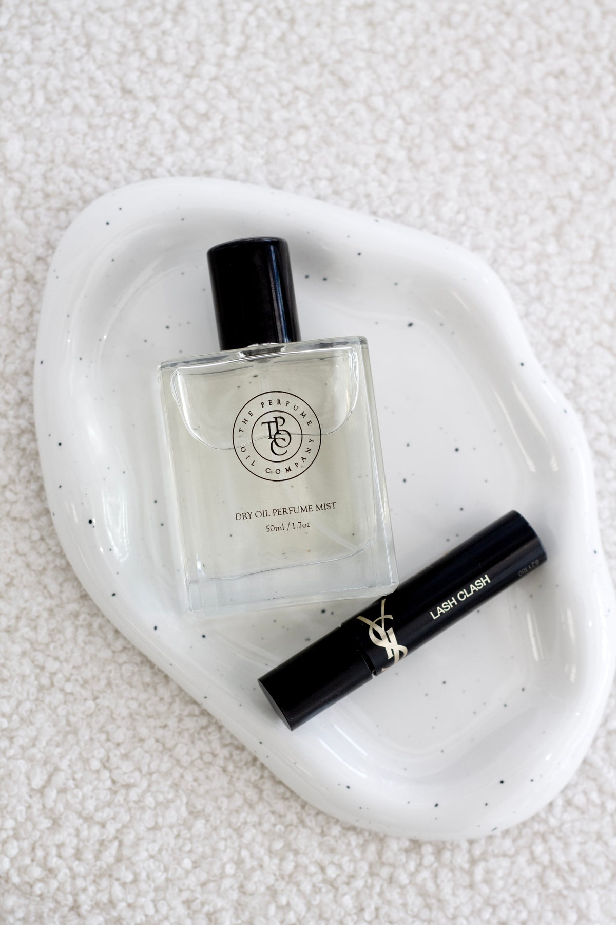 Speckled white cloud ceramic tray on boucle holding a perfume bottle and a mascara