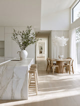 White Cloud Pendant paper lamp shade over a round timber dining table next to a marble kitchen island styled with olive branches