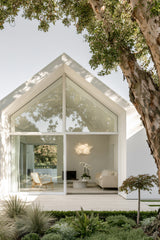 White Cloud Pendant paper lamp shade seen through the window of a modern gable home framed by trees
