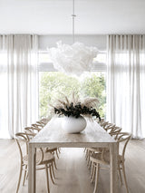 White sculptural paper cloud pendant lamp shade over timber dining table with bentwood chairs and pampas grass centrepiece