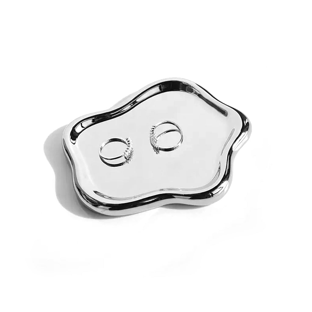 Silver mirrored cloud trinket dish holding two rings, on a plain background