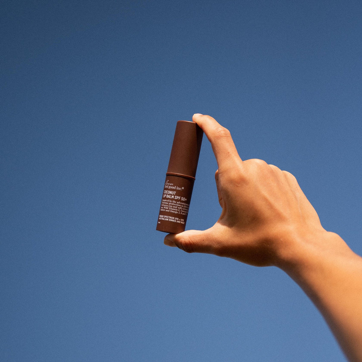 A person's hand holding a tube of We Are Feel Good Inc. Coconut Lip Balm SPF 50+.