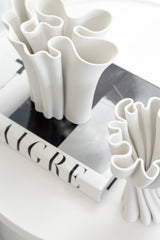 White sculptural 3D-printed vase with flowing wavy edges styled on a monochrome coffee table book in a minimal modern space.
