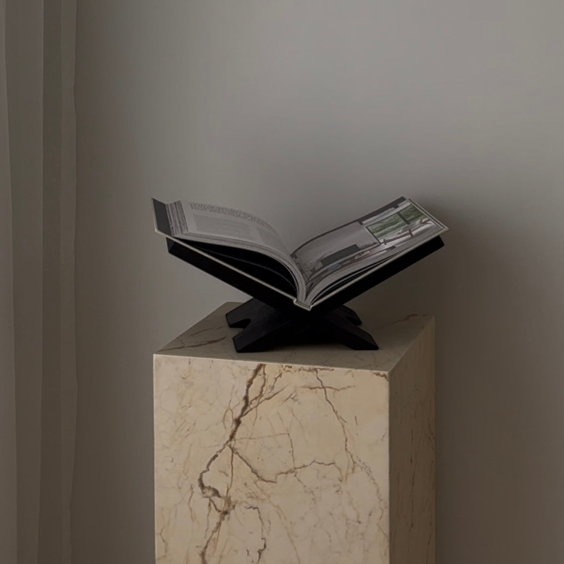Black Como book stand holding an open book on a marble plinth