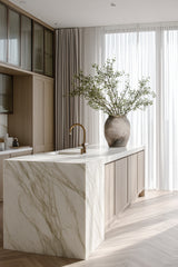 Large concrete-look bellied terracotta vase styled with tall greenery on marble kitchen island; sculptural statement decor.