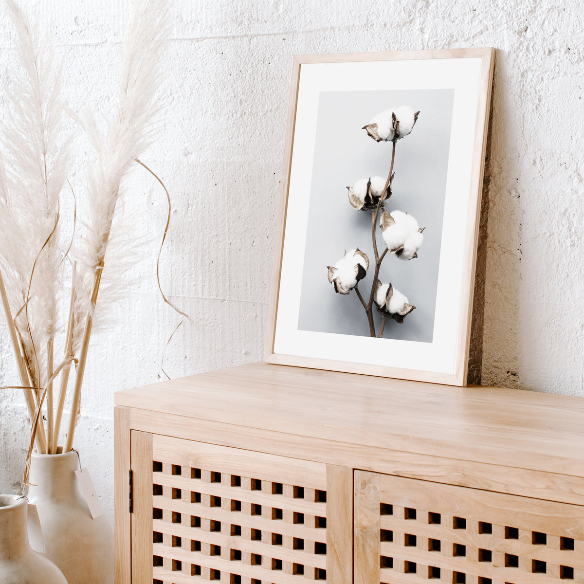 Cotton Flower print in a natural frame on a timber cabinet beside dried pampas