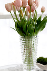 Clear cut glass vase with pink tulips styled on white table in soft natural light