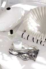 Large sculptural white ceramic wave bowl styled on a coffee table with marble accents and a perfume bottle.