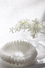 White resin and sand decorative wave bowl in soft window light alongside rippled glass pedestal vase with white orchid blooms