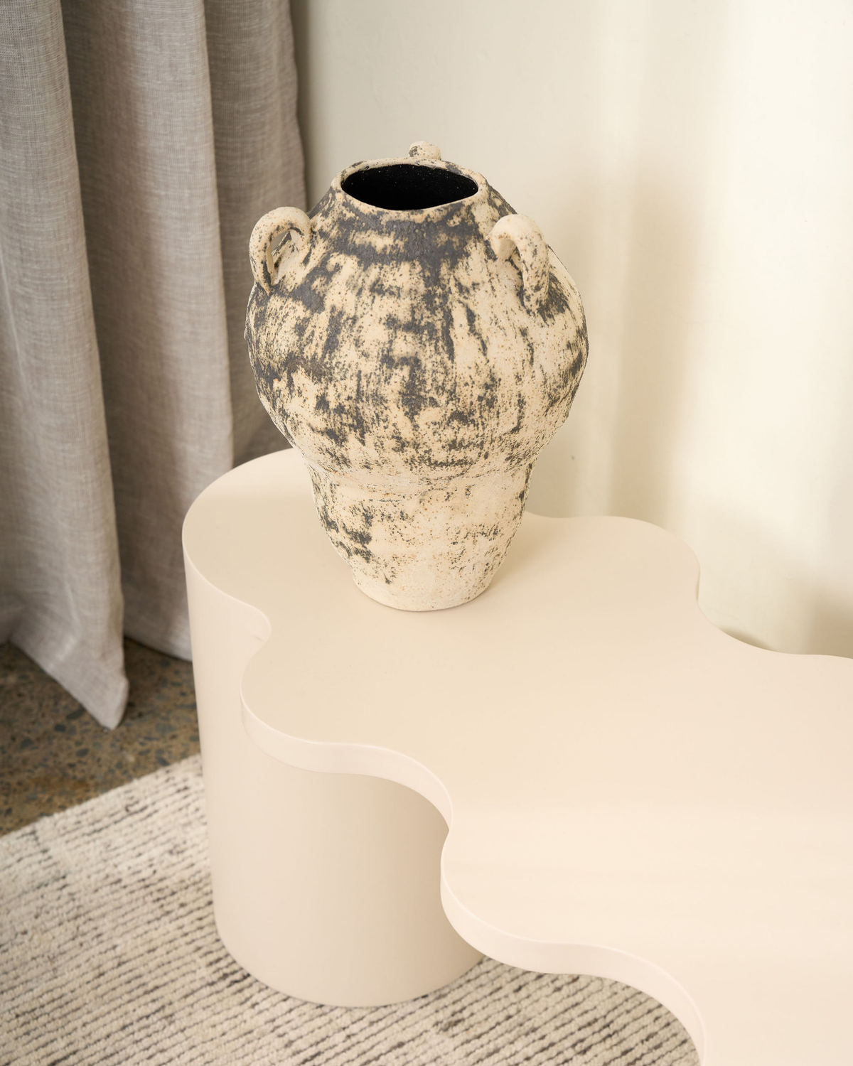 Close view of the Large vase on a cream wavy edged table, showing its handles and aged glaze
