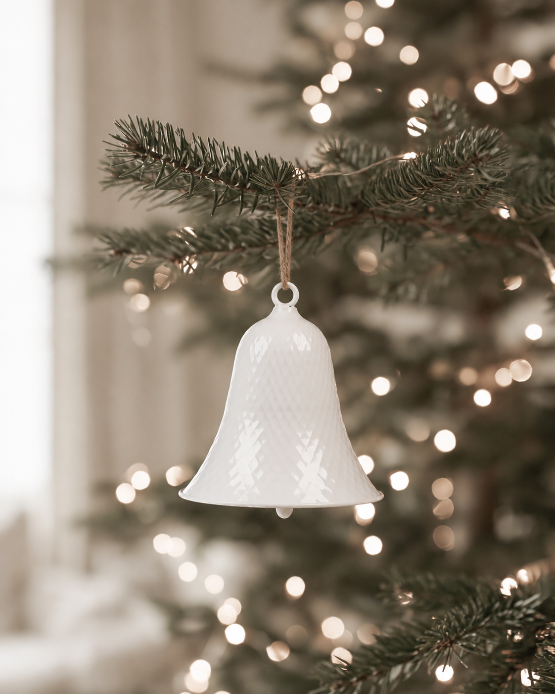 White enamel diamond texture bell hanging on twine from a lit Christmas tree branch
