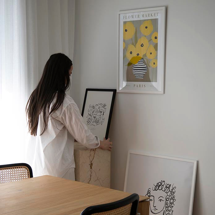 Dinner Party print in a black frame on a sideboard beside a woman and a dining table