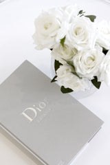 Dior Catwalk coffee table book with white roses in vase, styled in a minimal luxury flatlay for modern interiors
