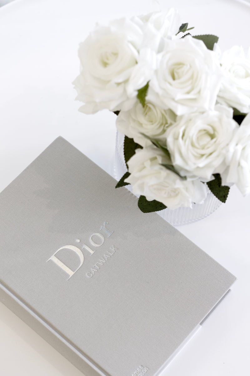 Dior Catwalk coffee table book with white roses in vase, styled in a minimal luxury flatlay for modern interiors