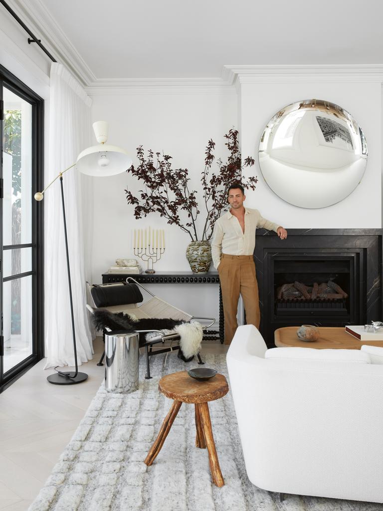 Man in a white living room beside a fireplace and round mirror