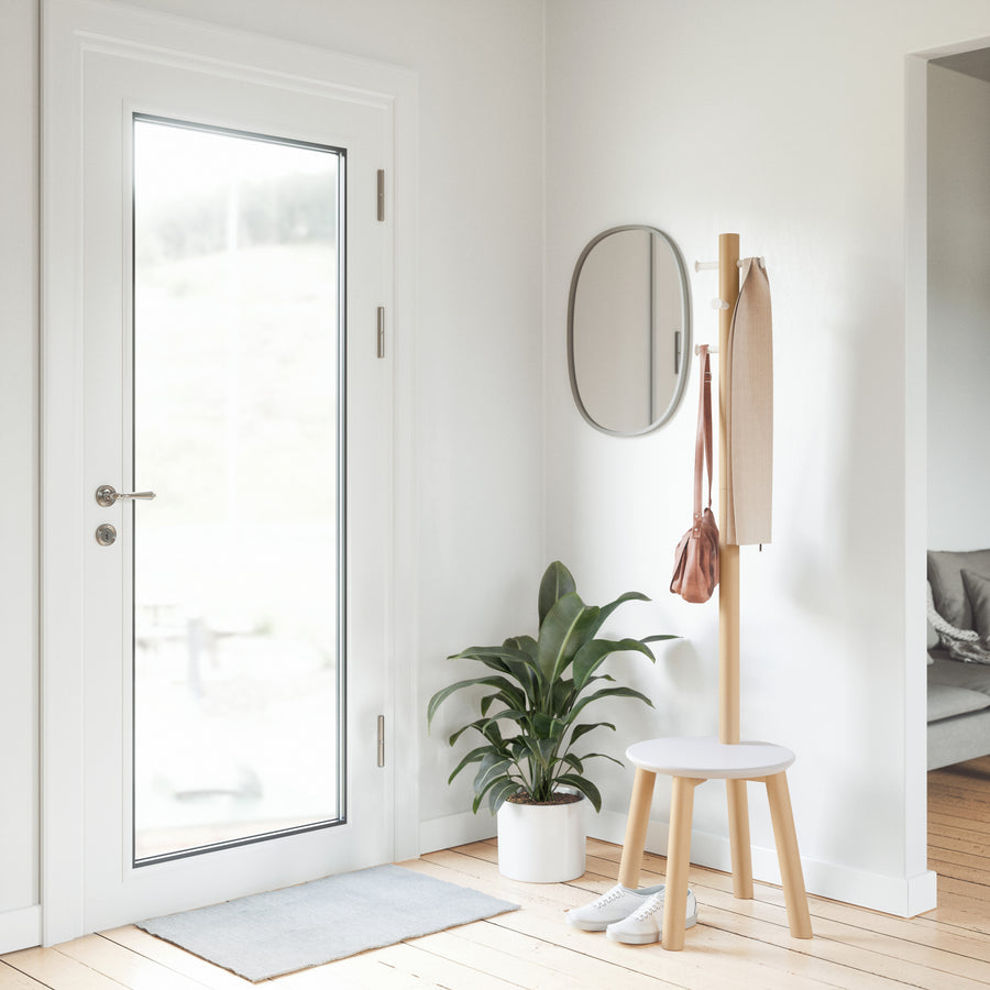 Umbra Pillar stool and coat rack in natural by a glass front door, coat on the hooks
