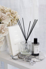 Ecoya Celebration Room Spray styled with faux florals, books, a ribbed diffuser bottle, and marble tray in soft neutral light.