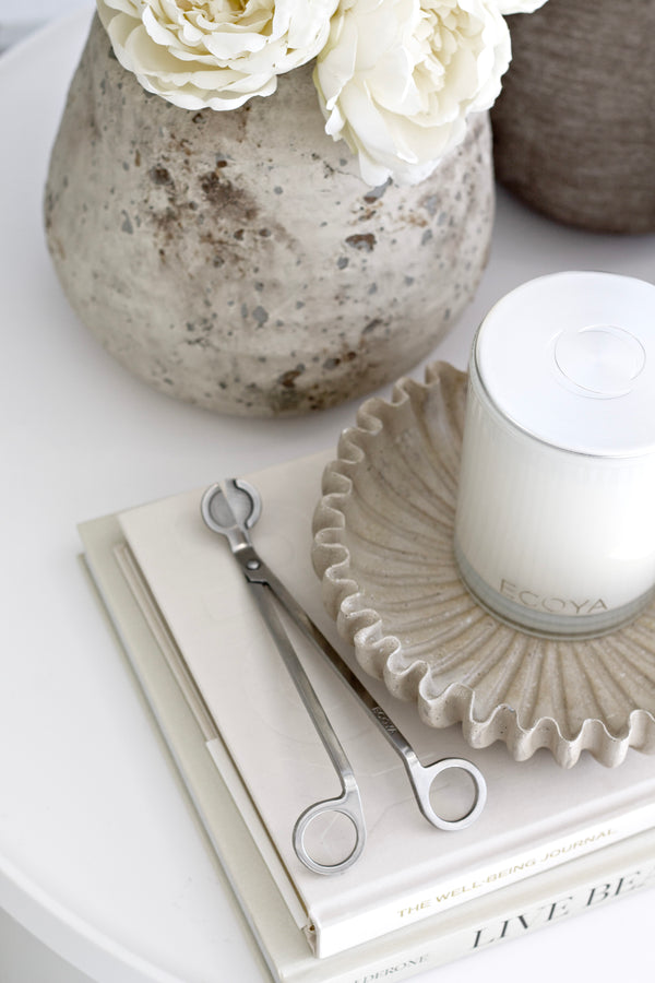 Ecoya stainless steel wick trimmer styled with candle and books on neutral coffee table.