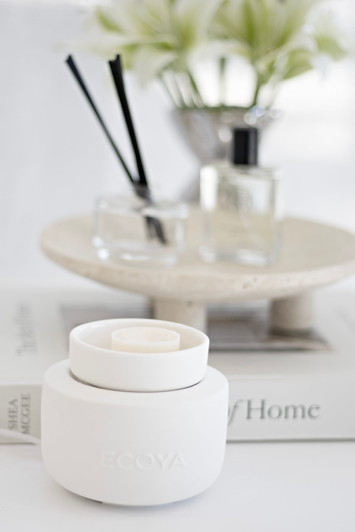 ECOYA Electric Wax Melter in white ceramic styled below a marble tiered tray with a reed diffuser and white flowers.