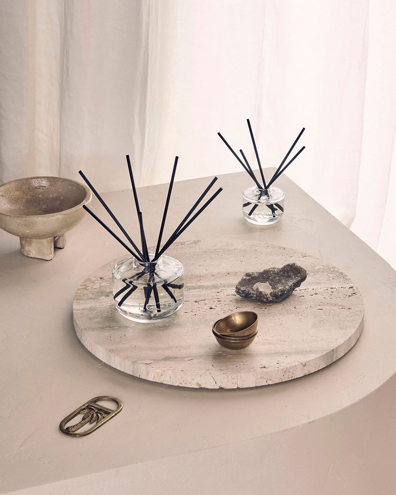 Ecoya reed diffusers styled on a travertine tray with sculptural decor in a soft neutral interior